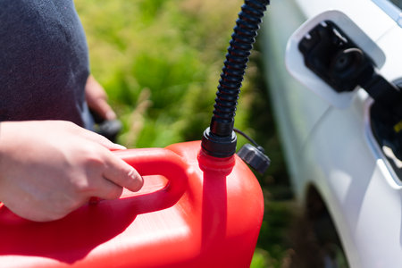 The driver fills up the empty tank of the car from a red canister on the side of the road. Fuel problem, force majeureの写真素材