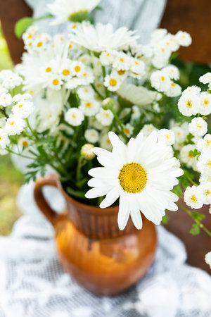 Beautiful chamomile flowers on a wooden old chair along with a lace doily on a green garden background. Summer atmosphere, simple home decor in the countryside. vertical photoの写真素材