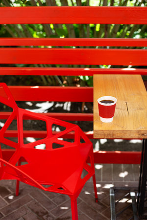 A wooden table on which there is a red plastic cup with coffee. Summer beautiful terrace in greenery. Cozy placeの写真素材