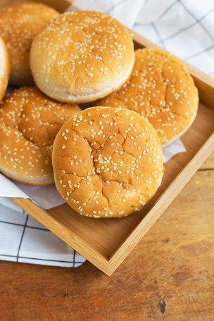 Freshly baked lush burger buns lie on a wooden tray on a table with a white napkin. Top view, close-up. Yellow flavored pastries with white sesame seedsの写真素材
