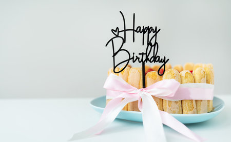 Strawberry tiramisu cake with cheese cream, decorated with a bow, the inscription Happy Birthday on top, a place for an inscriptionの写真素材
