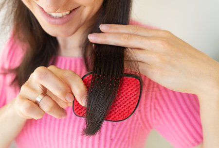 Portrait of a radiant girl combing her dark hair, looking away with a calm smile. hair care conceptの写真素材
