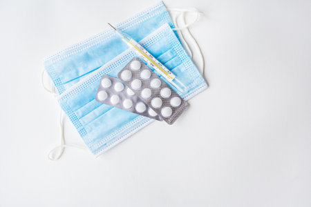 Preparation for vaccination against covid-19. Thermometer, pills, medical mask on a white table. Place for an inscriptionの写真素材