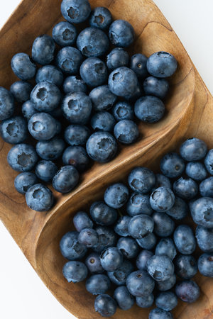 Ripe blueberries in a wooden interesting plate close-up on a white background. Delicious and healthy berry. View from aboveの写真素材