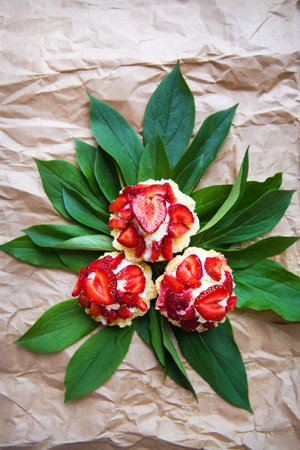 Beautiful and bright cupcakes with strawberries lie on green leaves, close-up.の写真素材