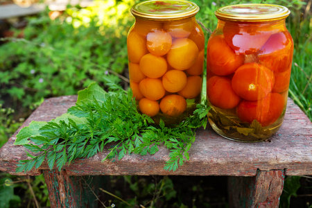 Tomatoes in a jar, delicious rosemary yellow and red tomatoes in a glass jar, the process of harvesting for the winter. Sunny dayの写真素材