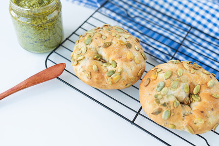 A freshly baked bagel with sunflower seeds lies on a metal stand along with a checkered napkin and a wooden knifeの写真素材