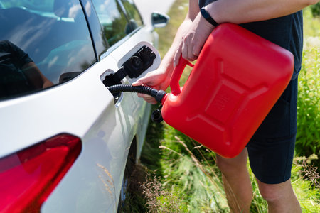 The driver fills up the empty tank of the car from a red canister on the side of the roadの写真素材