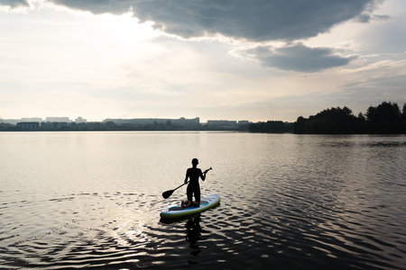 Water sports, surf lessons, the appearance of a girl against the backdrop of a sunrise. Stand on a kayak on the water with the warm colors of a summer sunsetの写真素材