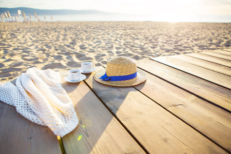 a hat, a cape and two cups of coffee stand on a pier near the sea.の写真素材