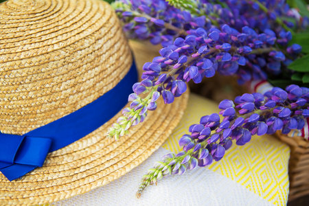 A hat, a plaid and a bouquet of lupines in a basket, close-up.の写真素材