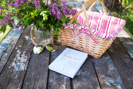 A basket, book, sunglasses and a beautiful bouquet of lilacs stands on an old table. Close-up.の写真素材