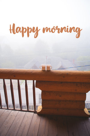 two cups of coffee standing on the balcony on a wooden house - the words of a happy morning.の写真素材