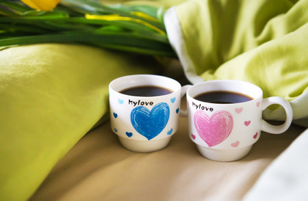 two cups of coffee stand on the bed with a bouquet of flowers, close-up.の写真素材