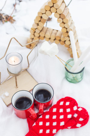 Picnic outside in winter. Christmas background, red mittens, red cups of coffee on snow, star candle. Merry christmas and a happy new yearの写真素材