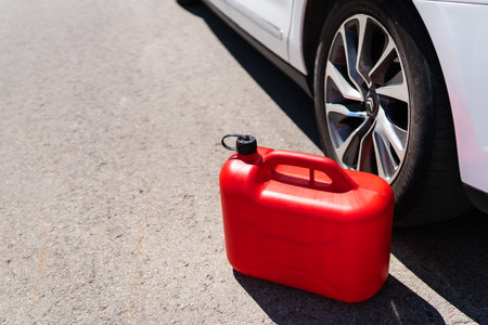 A red plastic can is in the middle of the road next to a white car. Refueling problemsの写真素材