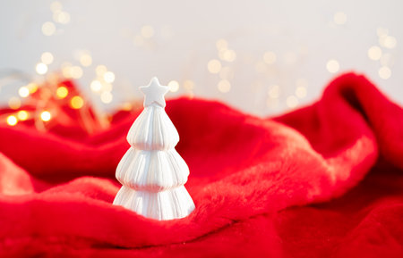 Christmas home interior with a white ceramic Christmas tree on a red plaid and bokeh with a garland in the background. Christmas and New Year conceptの写真素材