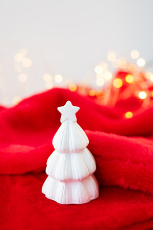 Christmas home interior with a white ceramic Christmas tree on a red blanket. Christmas and New Year concept. Vertical photoの写真素材