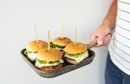 The cook holds a grill pan on which several juicy hamburgers lie and shows like. Interesting presentation. Delicious and fast foodの写真素材