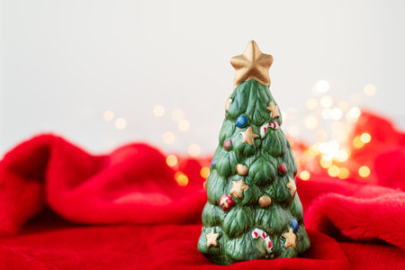 New Year's location with a green toy fir tree standing on a red blanket against a bokeh background with a garland of lights. Place for an inscriptionの写真素材