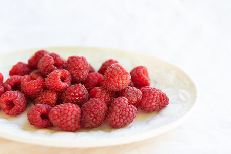 Fresh, ripe raspberries on a white plate, set against a white tablecloth. Perfect for a healthy...