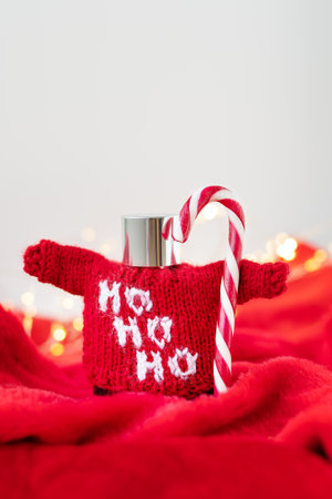 This is a. photo of a red sweater with Ho Ho Ho written on it, wrapped around a silver flask with a candy cane sticking out of it. The background is blurred with Christmas lights and a red blanketの写真素材