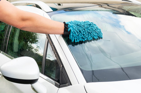 A person s hand with a blue microfiber mitt cleaning the windshield of a white carの写真素材