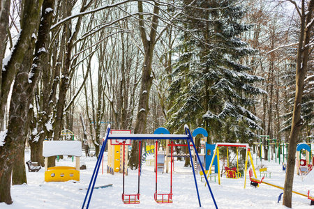 A quiet winter playground covered in snow, with colorful equipment and surrounded by bare evergreen treesの写真素材