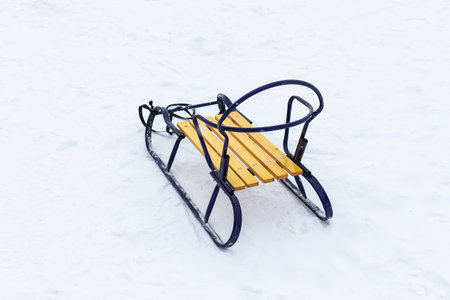 Wooden sleigh with blue metal frame and yellow seat on snowy surface, showing children's winter and outdoor gamesの写真素材