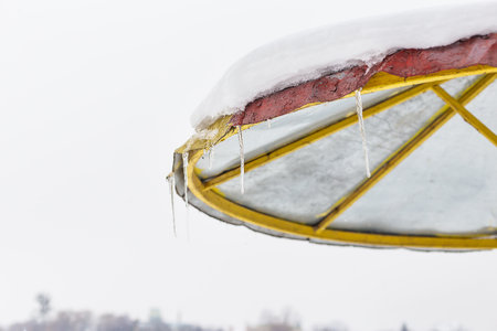 This image features a snow-covered umbrella with icicles hanging, against a blurred winter landscapeの写真素材
