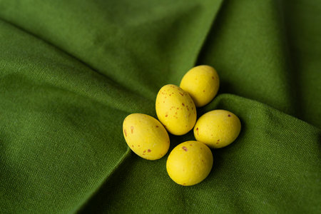 Five yellow speckled eggs on a folded green fabric with woven texture. Eggs with small brown spots, the combination of yellow eggs and green tissue creates a striking contrastの写真素材