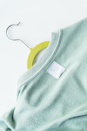 A close-up of a mint green sweater on a yellow hanger. The sweater has a visible texture and a white blank label. The background is plain and whiteの写真素材