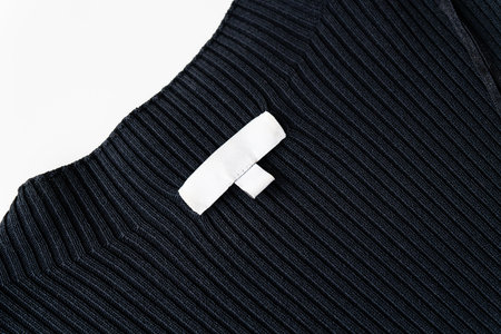 A black ribbed fabric garment with a white blank clothing label stitched onto it. The label is empty with no text or logoの写真素材