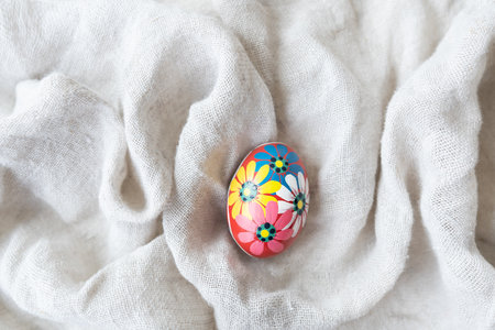 A colorful hand painted Easter egg with intricate floral designs on white fabric. The egg is...