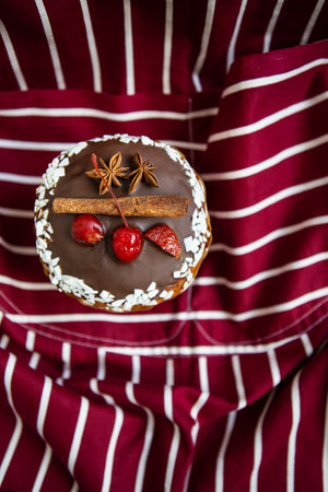 A traditional paska decorated with white and dark Swiss chocolate and cherries, cinnamon and star anise stands on a cherry striped apron. Easter holiday, top viewの写真素材