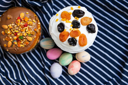 Delicious Easter cakes with colorful eggs on striped fabric. Two cakes, one with white frosting, the...