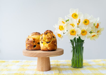 Fresh pastries on a wooden stand combined with a bright bouquet of daffodils on a checkered tablecloth. Easterの写真素材