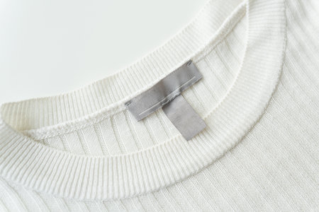 Close-up of a white knitted sweater neckline with a gray tag, highlighting fabric texture and qualityの写真素材