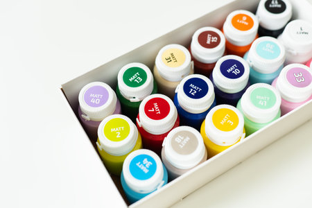 A box of colorful paint bottles, neatly arranged, showing vibrant hues. Labels on caps indicate paint colorsの写真素材