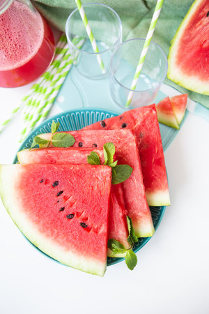 Fresh watermelon slices on a blue plate, garnished with mint, next to a refreshing smoothie and whole fruitの写真素材