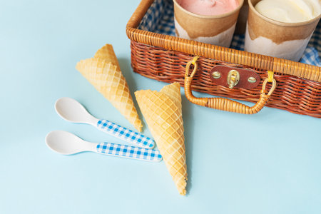 The image shows ice cream cones and cups in a wicker picnic basket against a blue background. The...