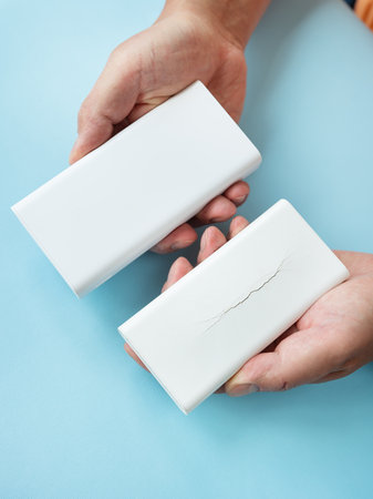 Hands comparing a new and a cracked power bank on a blue backgroundの写真素材