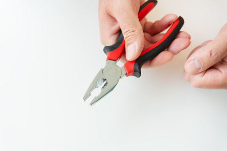 A hand firmly gripping red and black pliers against a white background