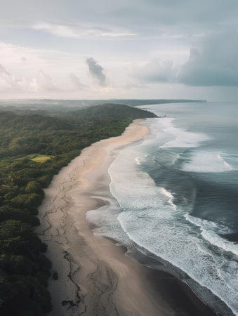 As dusk sets in, the shoreline is a serene retreat with frothy waves gently lapping the sand and lush greenery standing guard. The overcast sky suggests the tranquil end to a day in paradiseの素材