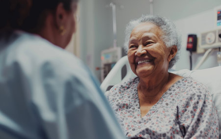An elderly woman in a floral hospital gown beams with a radiant smile, her joyful expression engaging the person sitting opposite herの素材