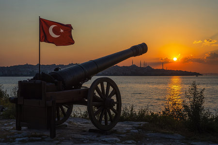 Silhouette of cannon with Turkish flag against Istanbul skyline at dusk.の素材