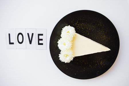 creamy cheesecake on a black plate decorated with white flowers-inscription love.の写真素材