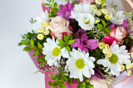 A beautiful bouquet of fresh flowers in pastel colors, including roses, daisies, and alstroemerias, arranged in a basket.の写真素材