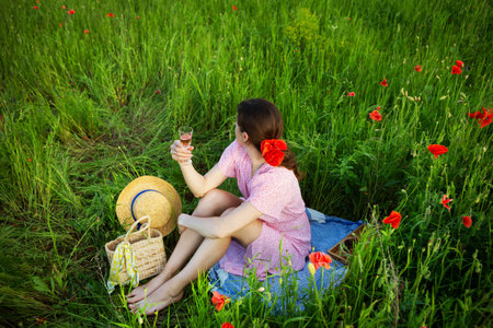 A woman enjoys a picnic in a vibrant poppy field, raising a glass of rose wine.の写真素材