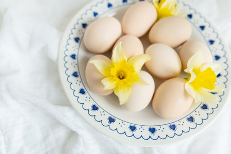 Pastel-colored eggs nestled amongst delicate daffodils on a charming blue and white plate. A perfect springtime Easter image, symbolizing new beginnings and celebration.の写真素材